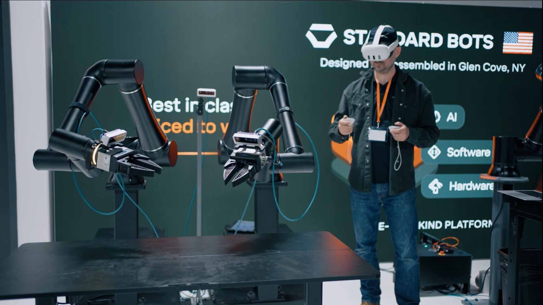 A person wearing VR goggles operates robotic arms at a tech exhibit. A screen in the background displays "Standard Bots."