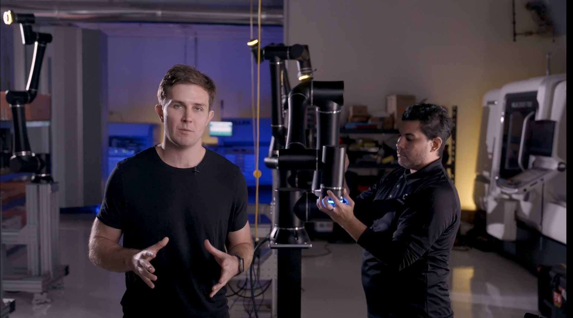 Two people in a tech lab: Two people Evan Beard CEO, the other adjusting equipment. Machines and blue lighting in the background.
