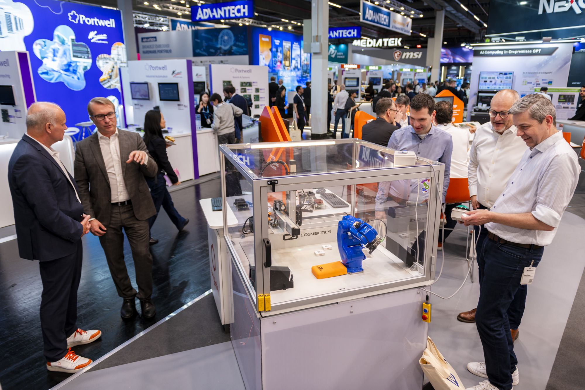 People interact at a congatec Embedded world booth featuring a robotic arm. Various company displays and attendees are visible in the background.