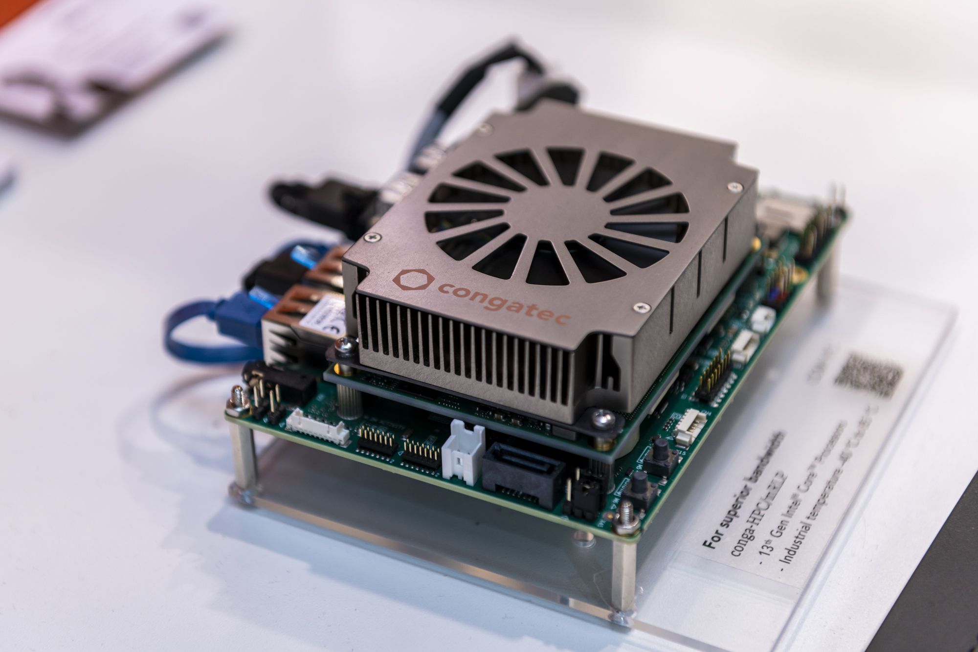 A congatec computer module with a prominent heatsink and cooling fan on a circuit board, displayed on a table with Cognibotics real time motion stack on