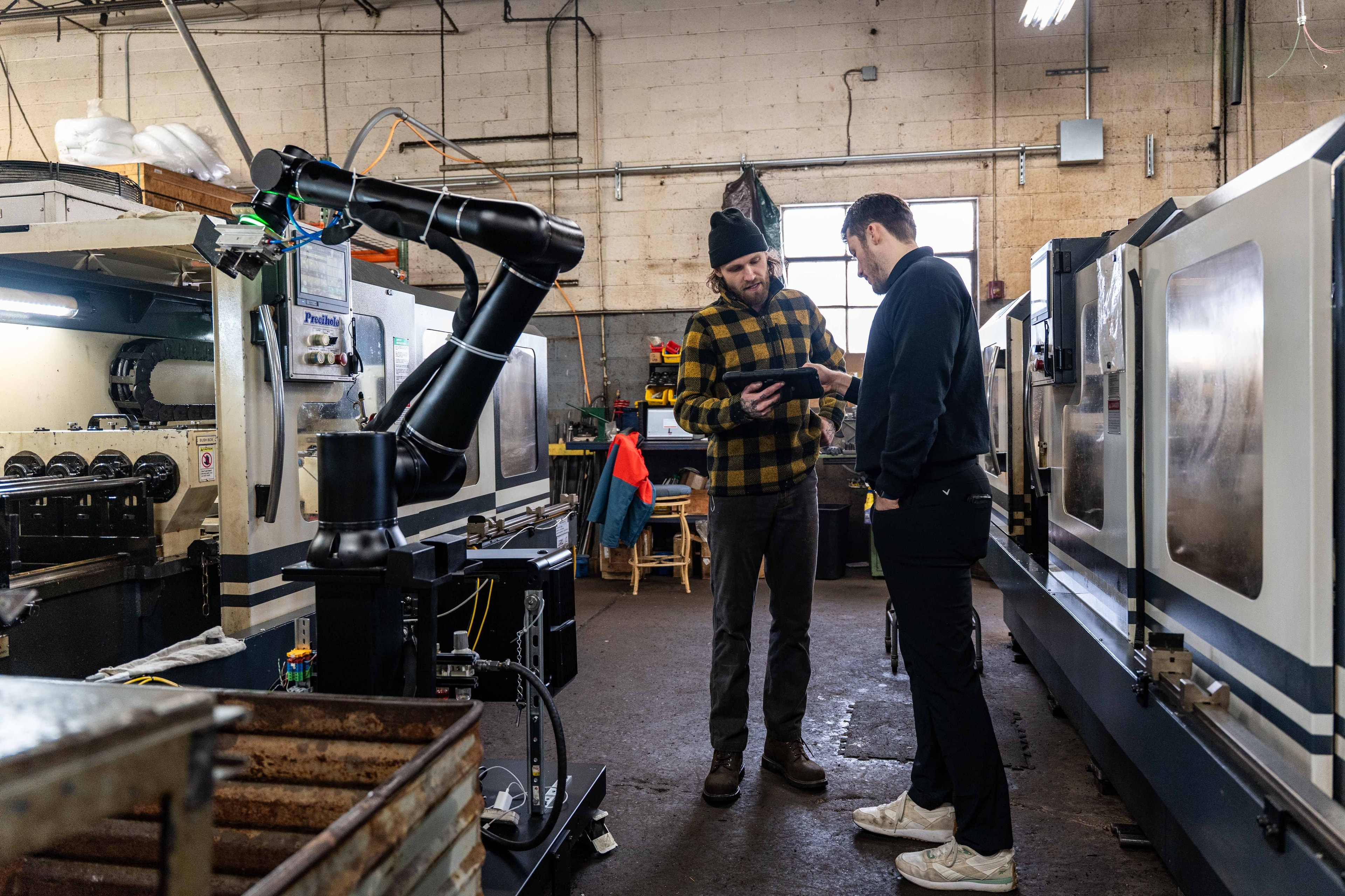 Two people in a workshop with machinery, discussing while one holds a tablet